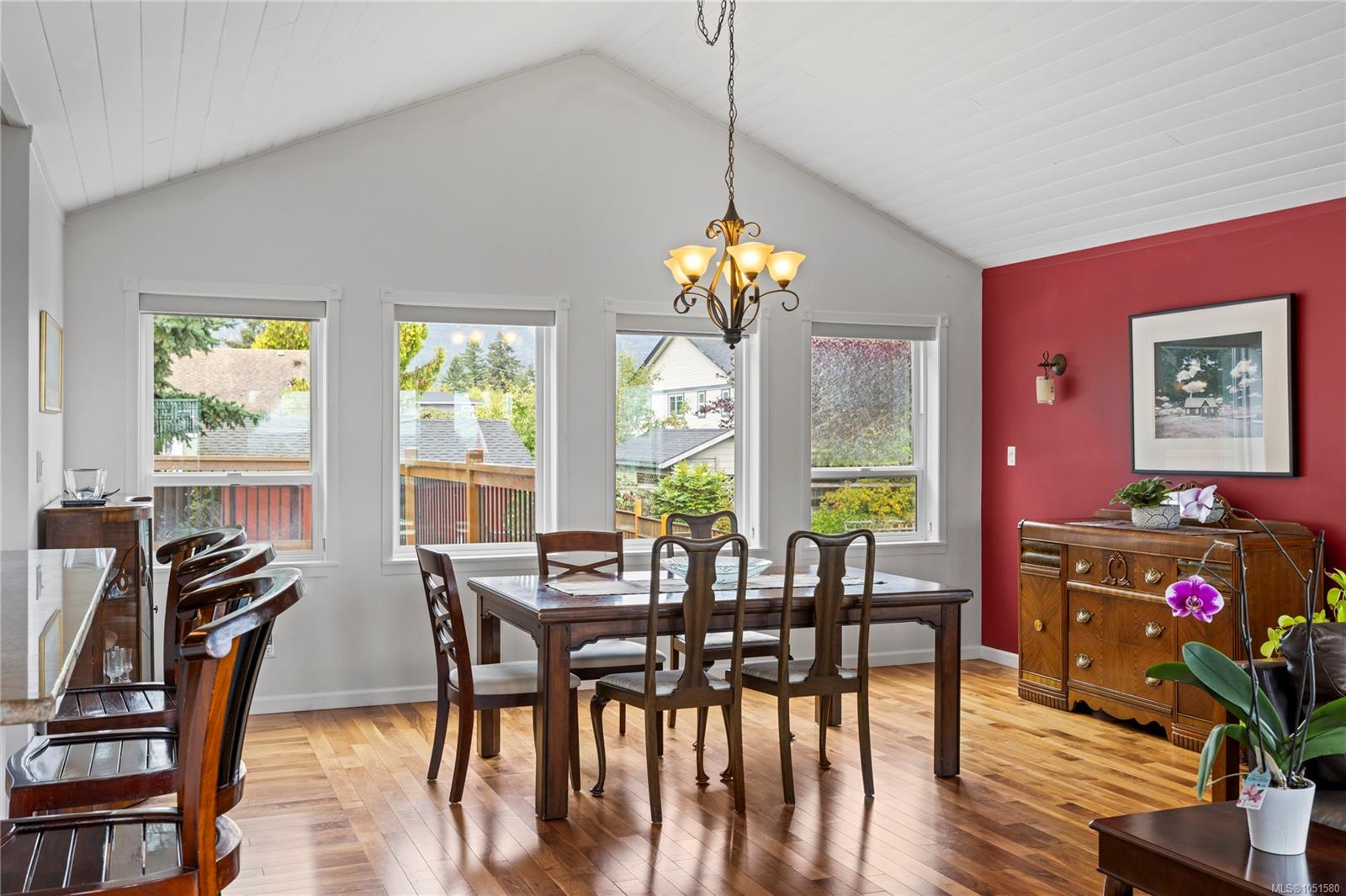 Dining room with a vaulted ceiling, red accent wall, and large windows overlooking the deck.