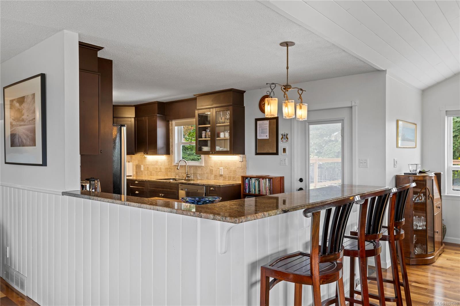 Kitchen with dark wood cabinets, granite breakfast bar, and wooden bar stools.