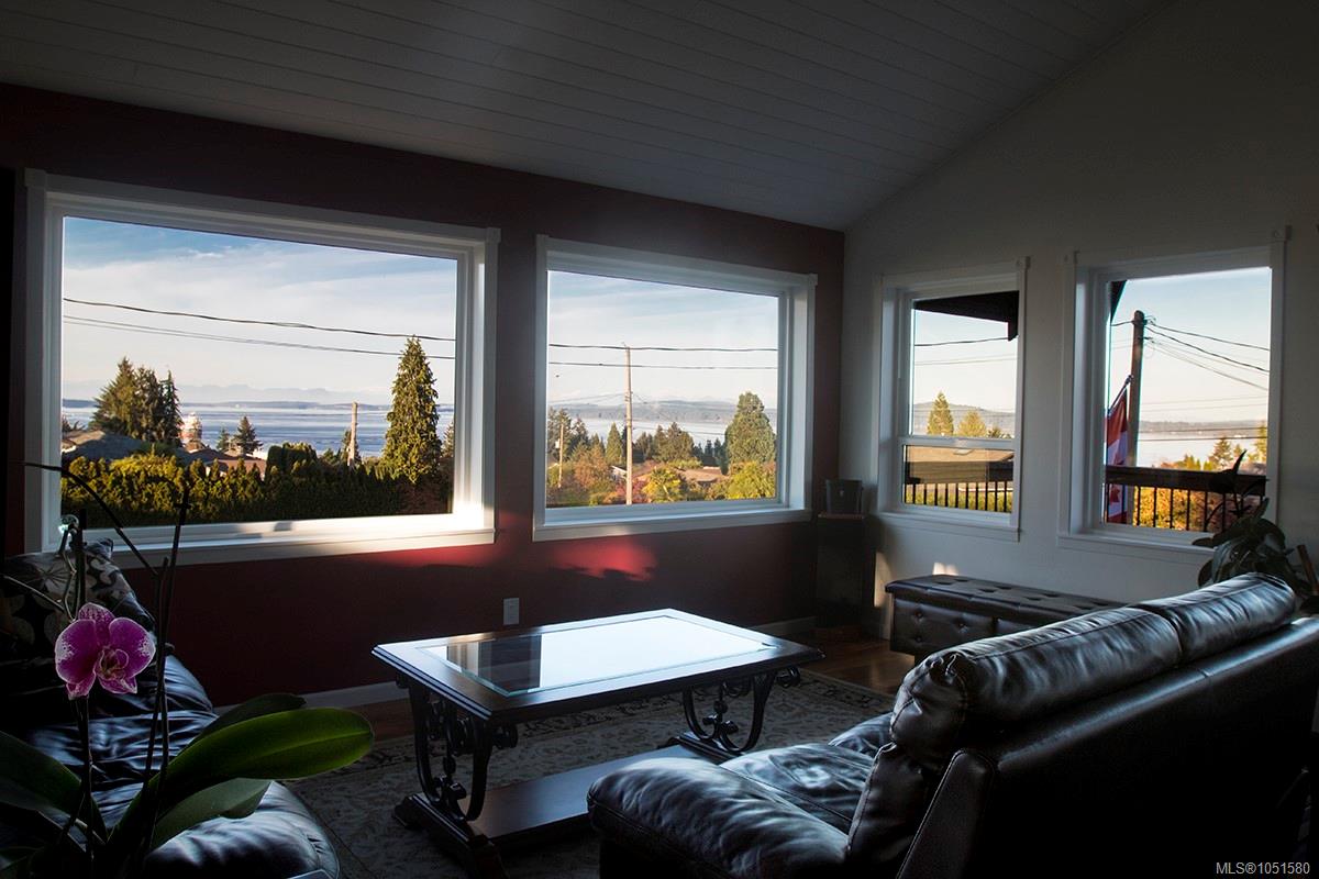 Furnished living room with large windows overlooking the water and distant shoreline.