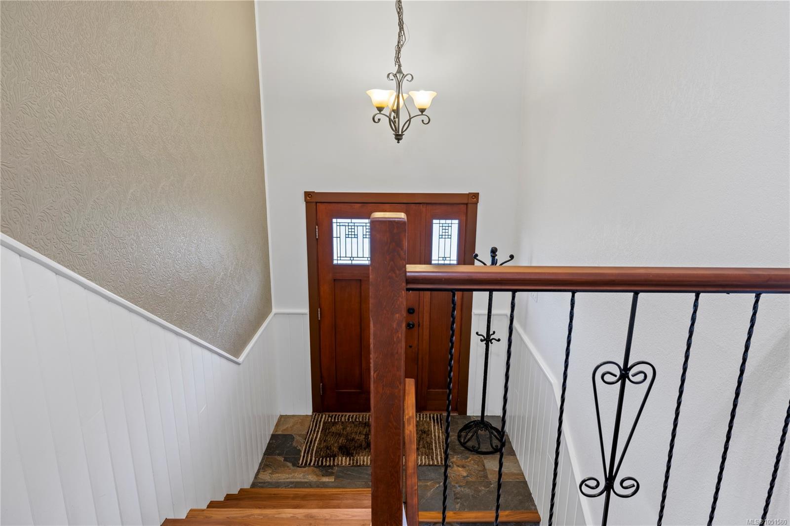 Entry staircase with a wood-and-iron railing leading down to a front door with decorative glass.
