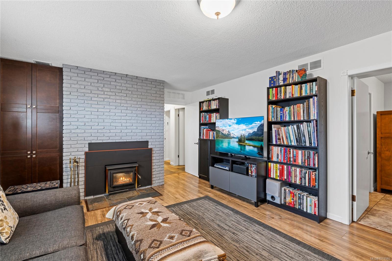 Living room with a white brick fireplace, wood stove, bookshelves, and television.