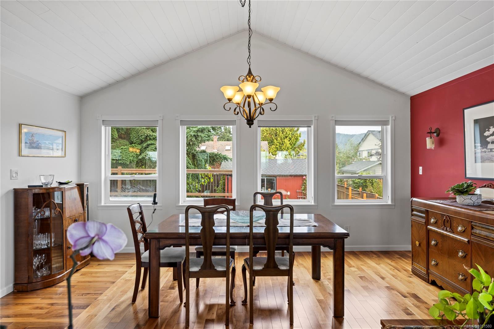 Dining room with a vaulted ceiling, chandelier, hardwood floors, and windows overlooking the yard.