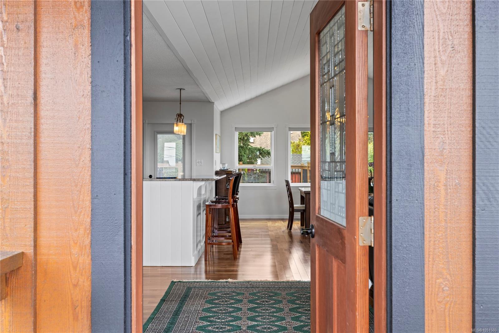 Open front door reveals a bright dining area with a vaulted ceiling and wood floors.