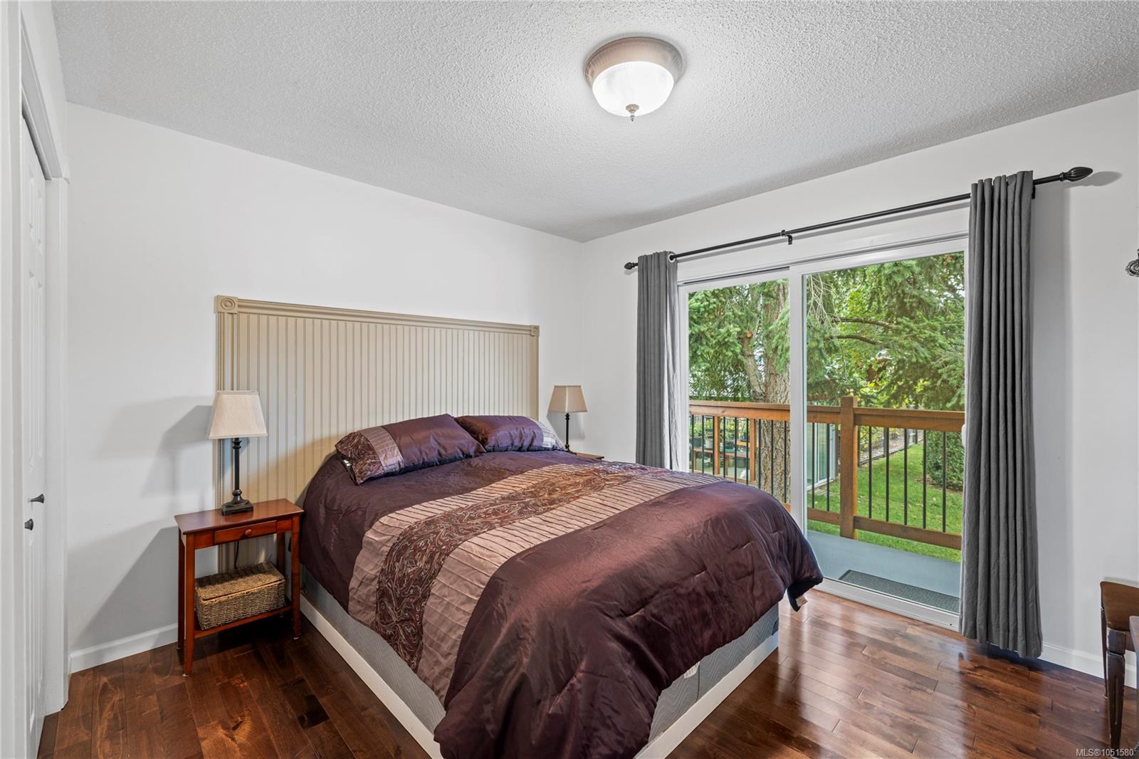 Bedroom with a dark plum bedspread beside sliding glass doors opening onto a wooded deck.