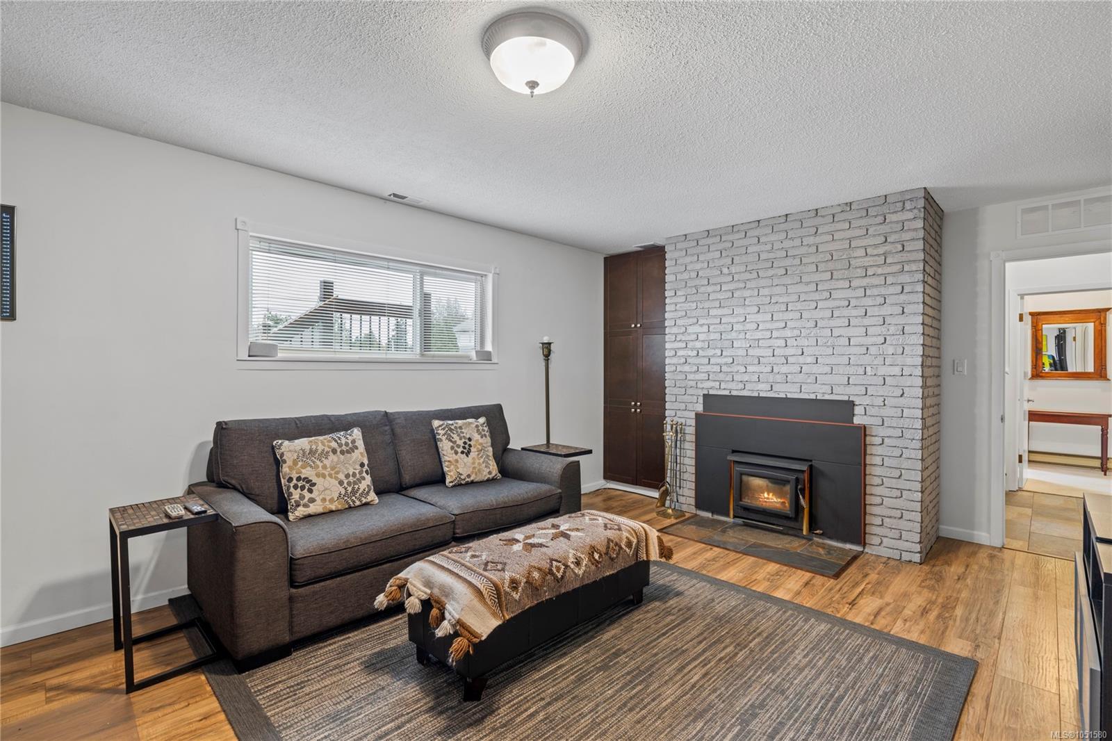 Living room with a gray sofa, white brick fireplace, and wood floors.