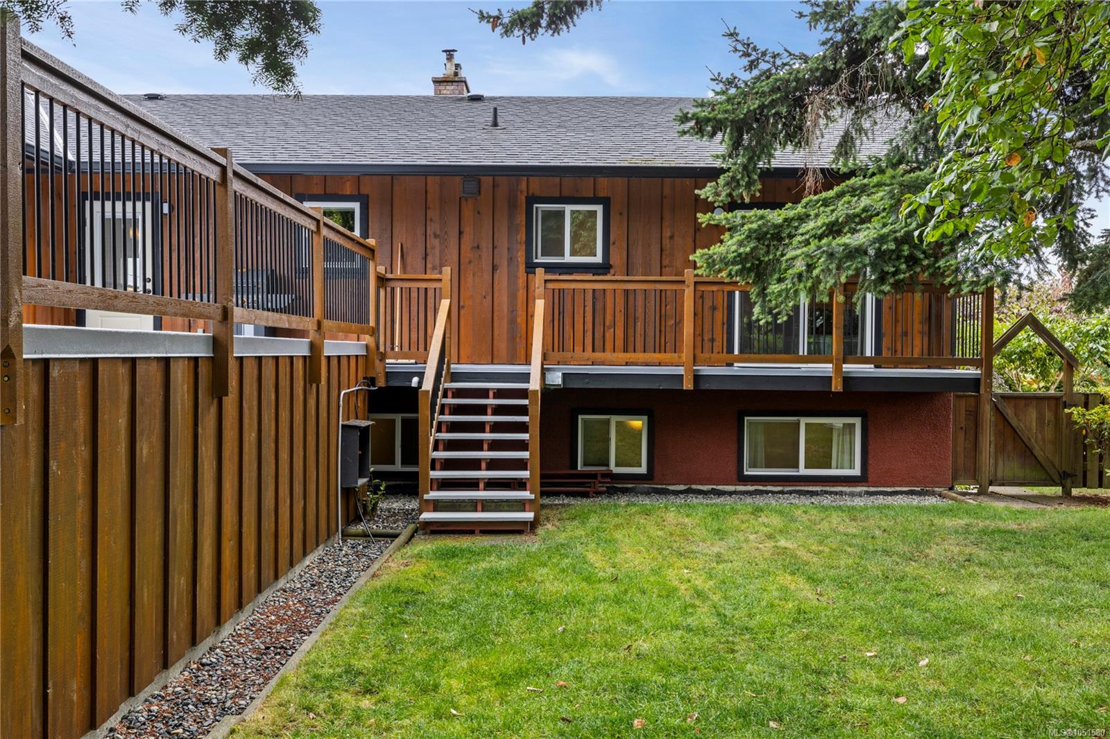 Wood-sided home with a raised deck, exterior stairs, and fenced grassy yard.