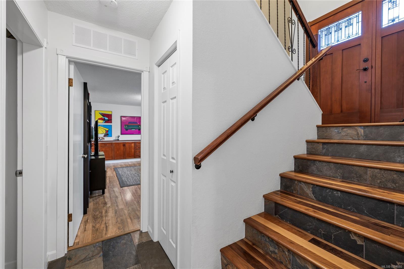Entry foyer with stone-tiled stairs, wooden handrail, and a paneled front door with decorative glass.
