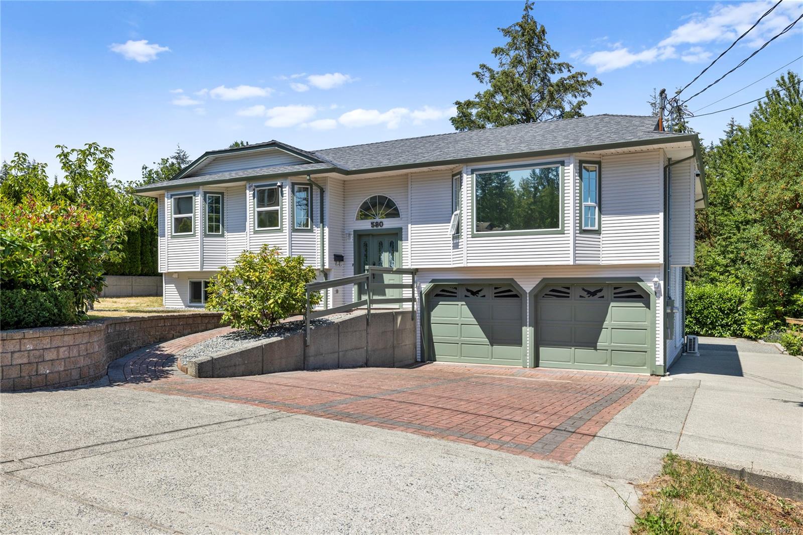 Raised-entry house with light siding, a two-car garage, and a brick-paved driveway.