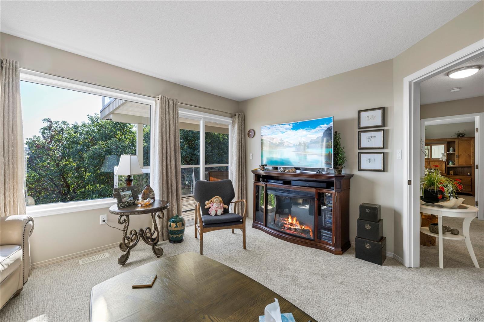 Living room with a dark wood fireplace, large windows, and views of greenery.