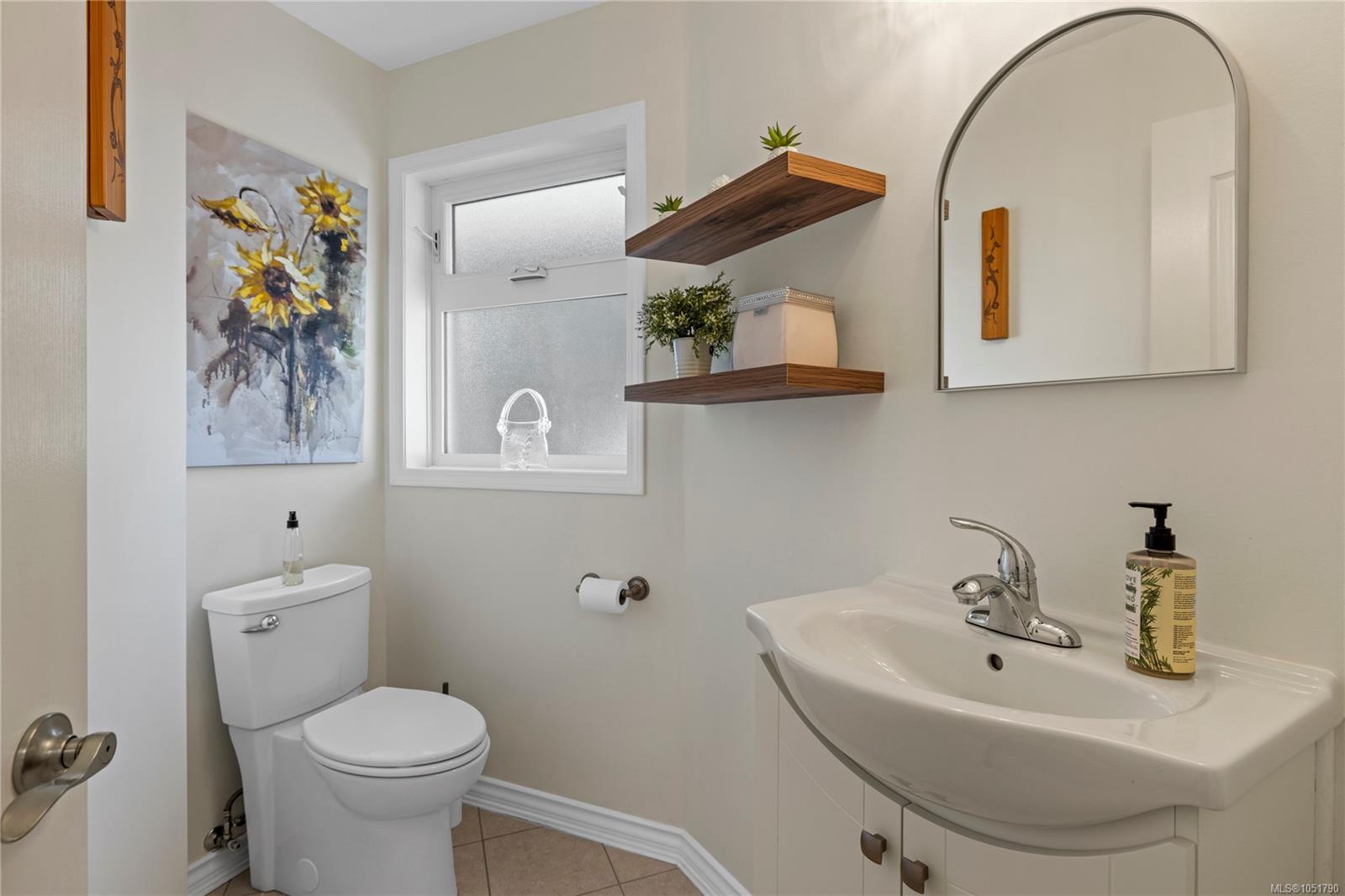 Bathroom with white toilet and sink vanity, arched mirror, and floating wood shelves.