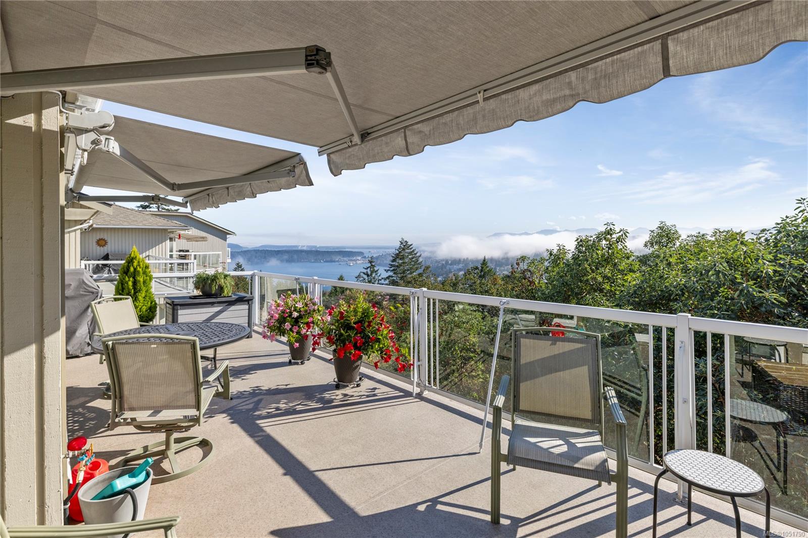 Deck with retractable awnings, glass railing, flower planters, and a view of water and distant mountains.