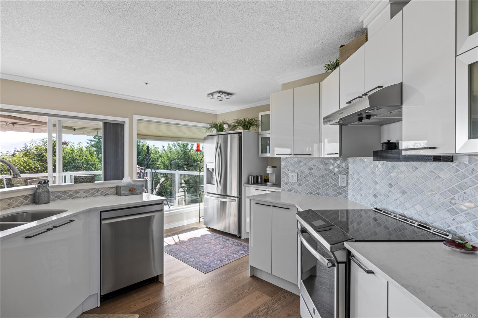 Modern white kitchen with stainless steel appliances and large windows overlooking greenery.