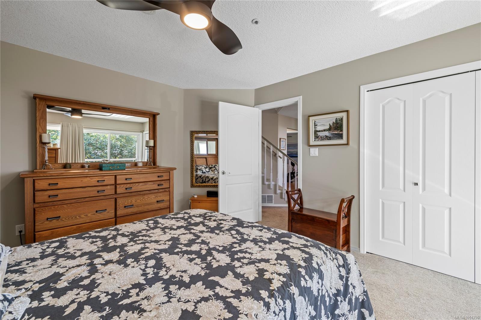 Bedroom with a dark floral bedspread, wooden dresser and mirror, ceiling fan, and white closet doors.