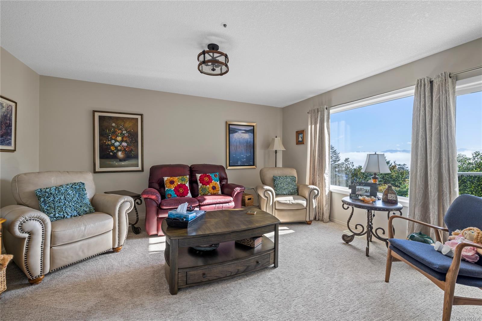 Furnished living room with a burgundy loveseat, cream armchairs, and a window overlooking distant mountains.