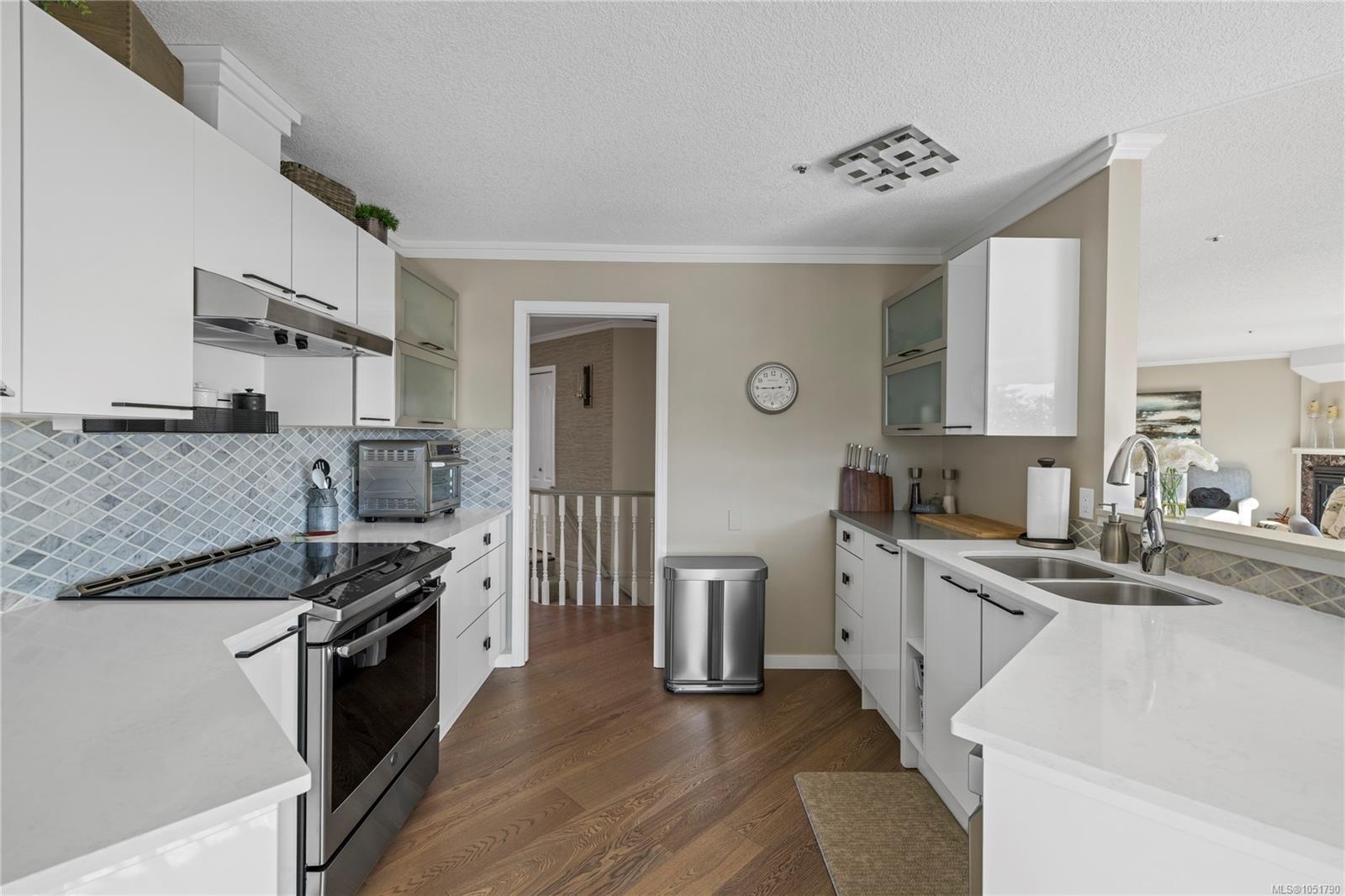Bright kitchen with white cabinetry, gray tile backsplash, stainless steel range, and double sink.