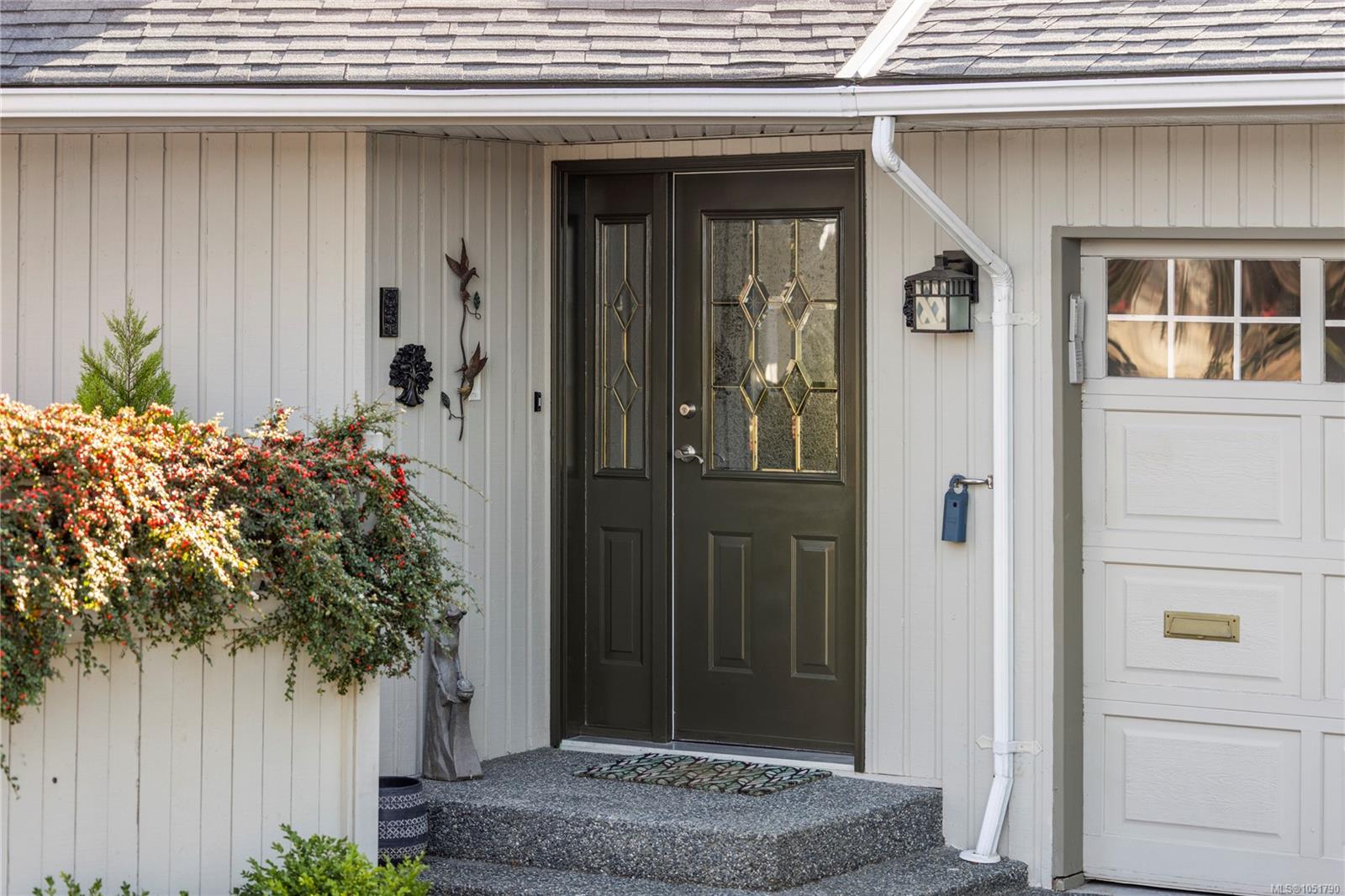 Front entrance with a dark decorative-glass door, covered porch, flowering shrubs, and attached garage.