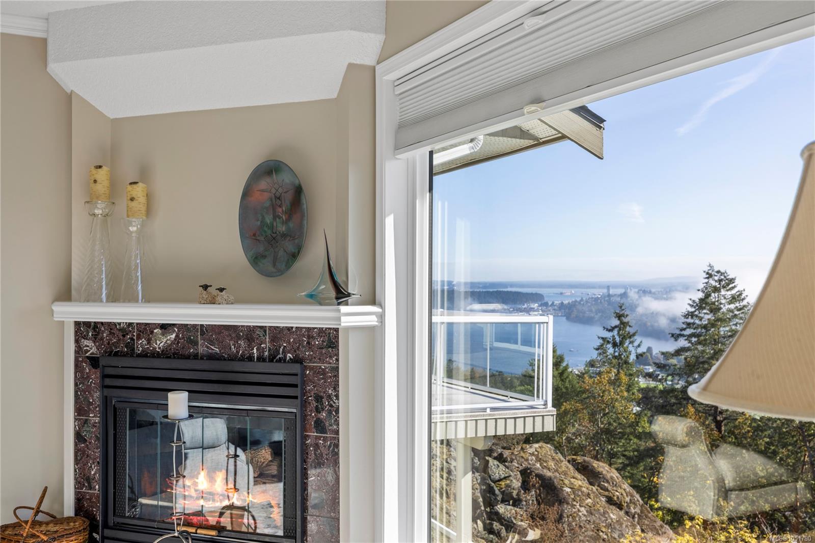 Living room fireplace beside a large window overlooking water and wooded shoreline.