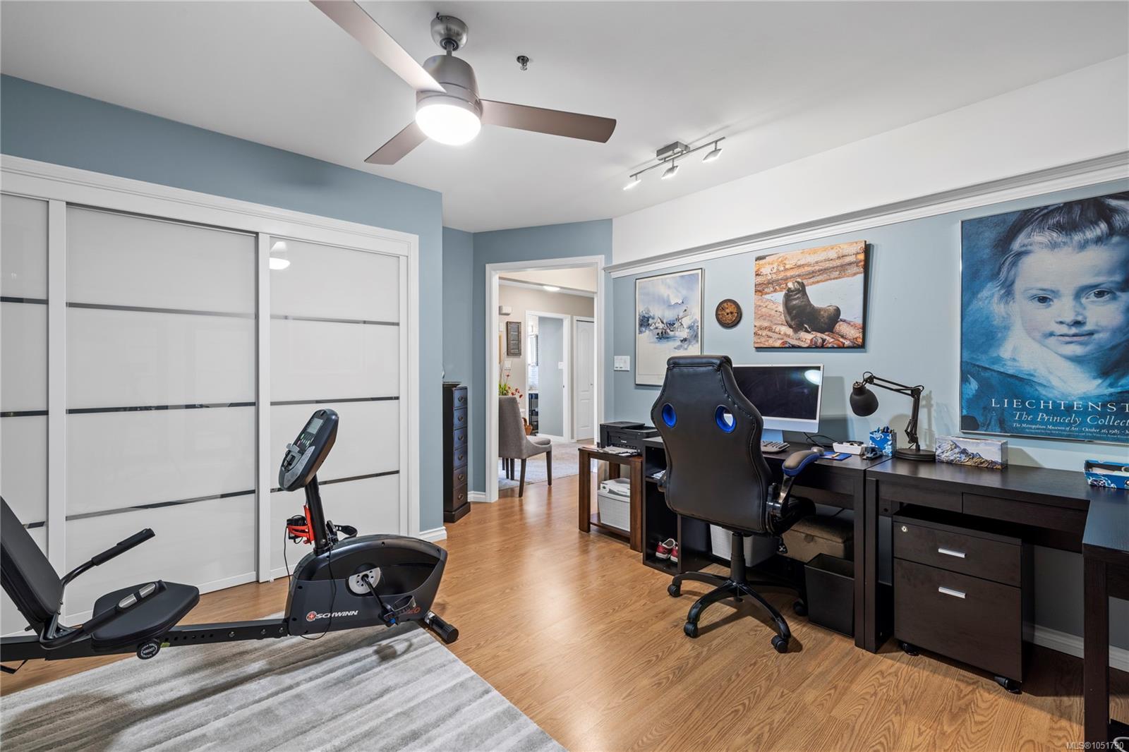 Home office with a desk and gaming chair, exercise bike, and white sliding closet doors.