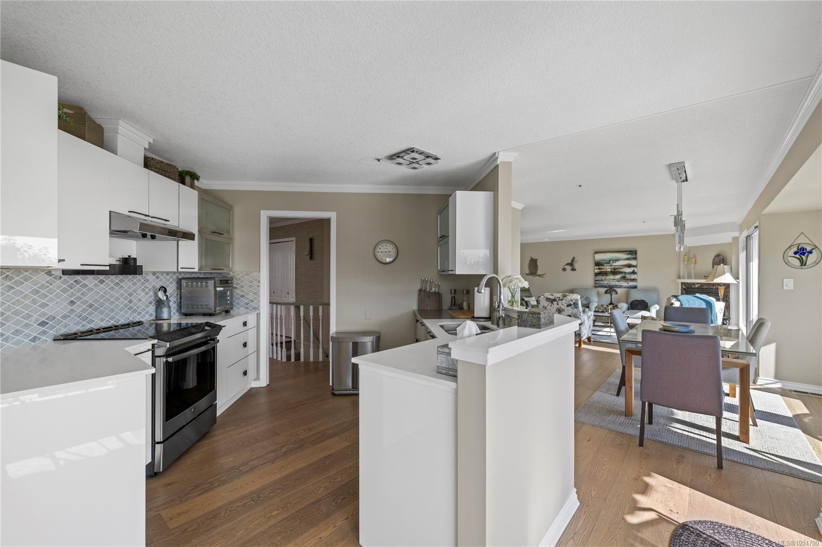 Open-plan kitchen with white cabinets and peninsula leading to a furnished dining and living area.
