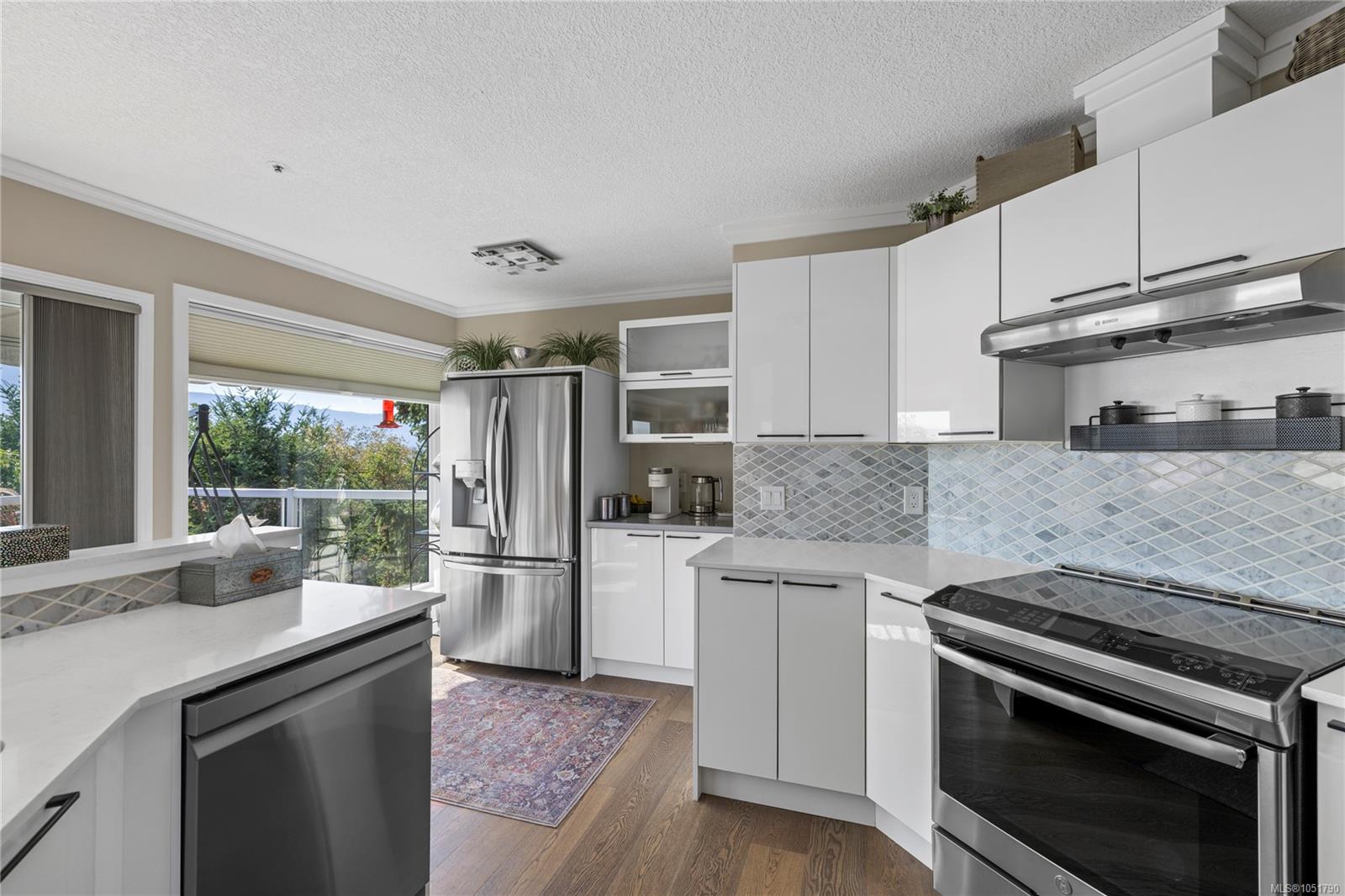 Kitchen with white cabinets, stainless steel appliances, patterned tile backsplash, and a window overlooking greenery.