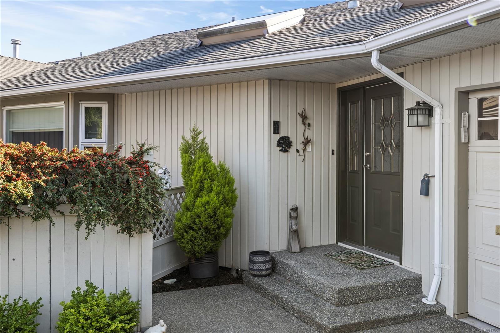 Covered home entrance with dark double doors, concrete steps, and flowering shrubs.