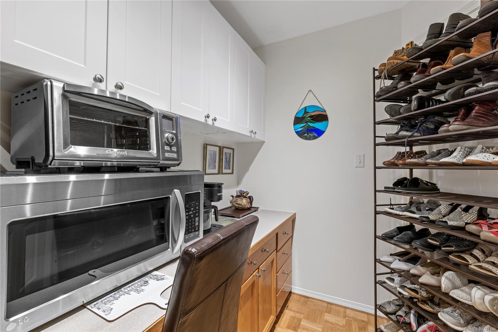 Storage room with wood cabinetry, stainless-steel appliances, and a tall rack filled with shoes.