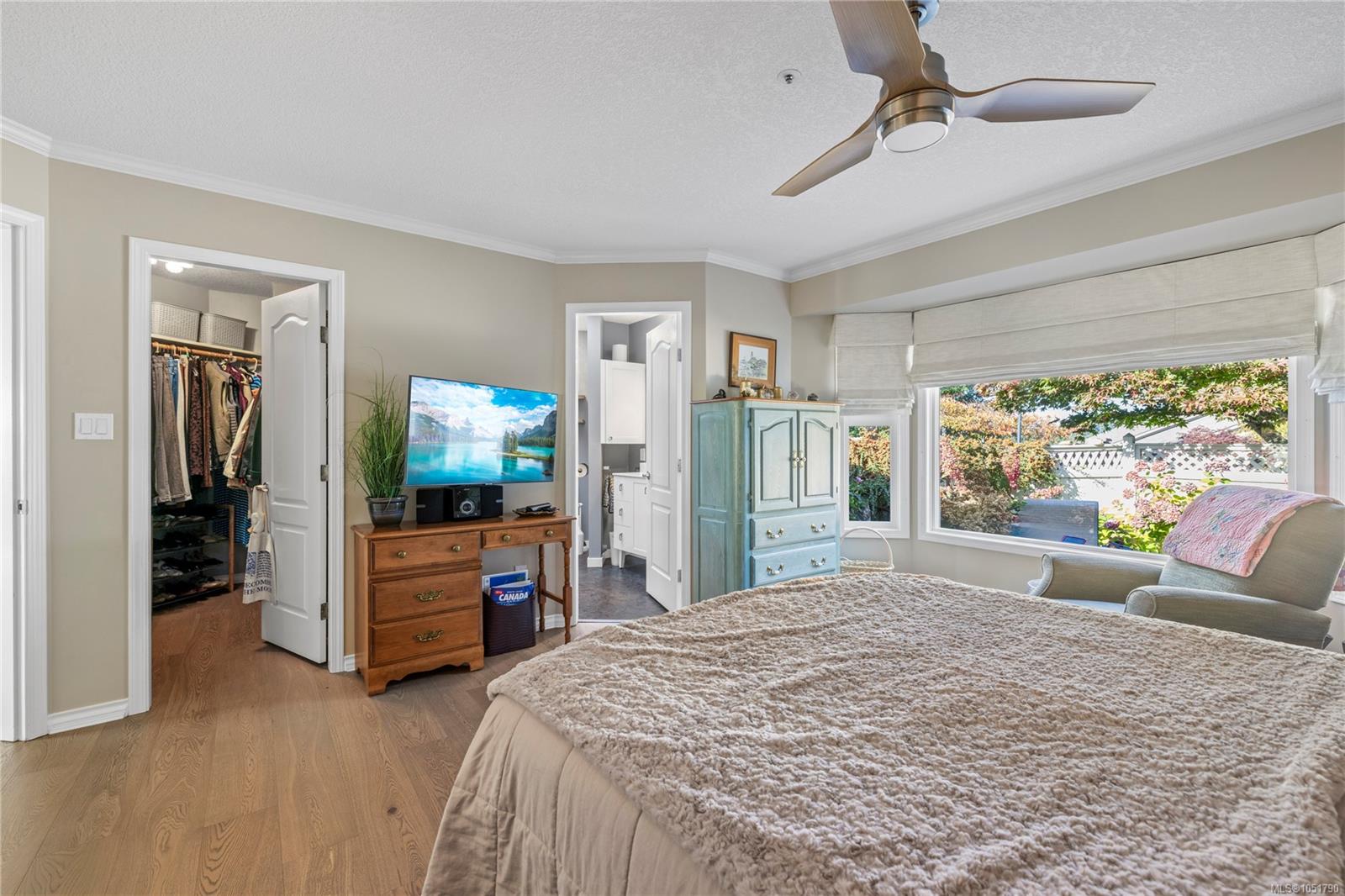 Furnished bedroom with a ceiling fan, walk-in closet, and wide garden-facing window.