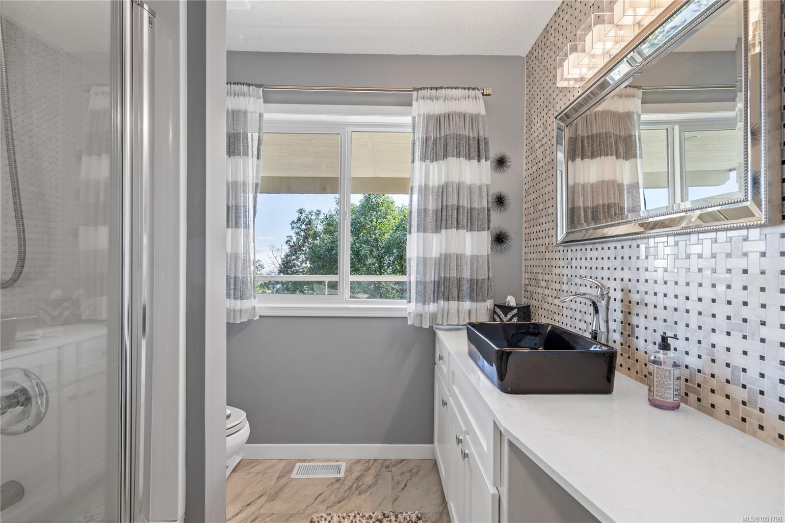 Bathroom with a black vessel sink, patterned tile backsplash, and window with striped curtains.