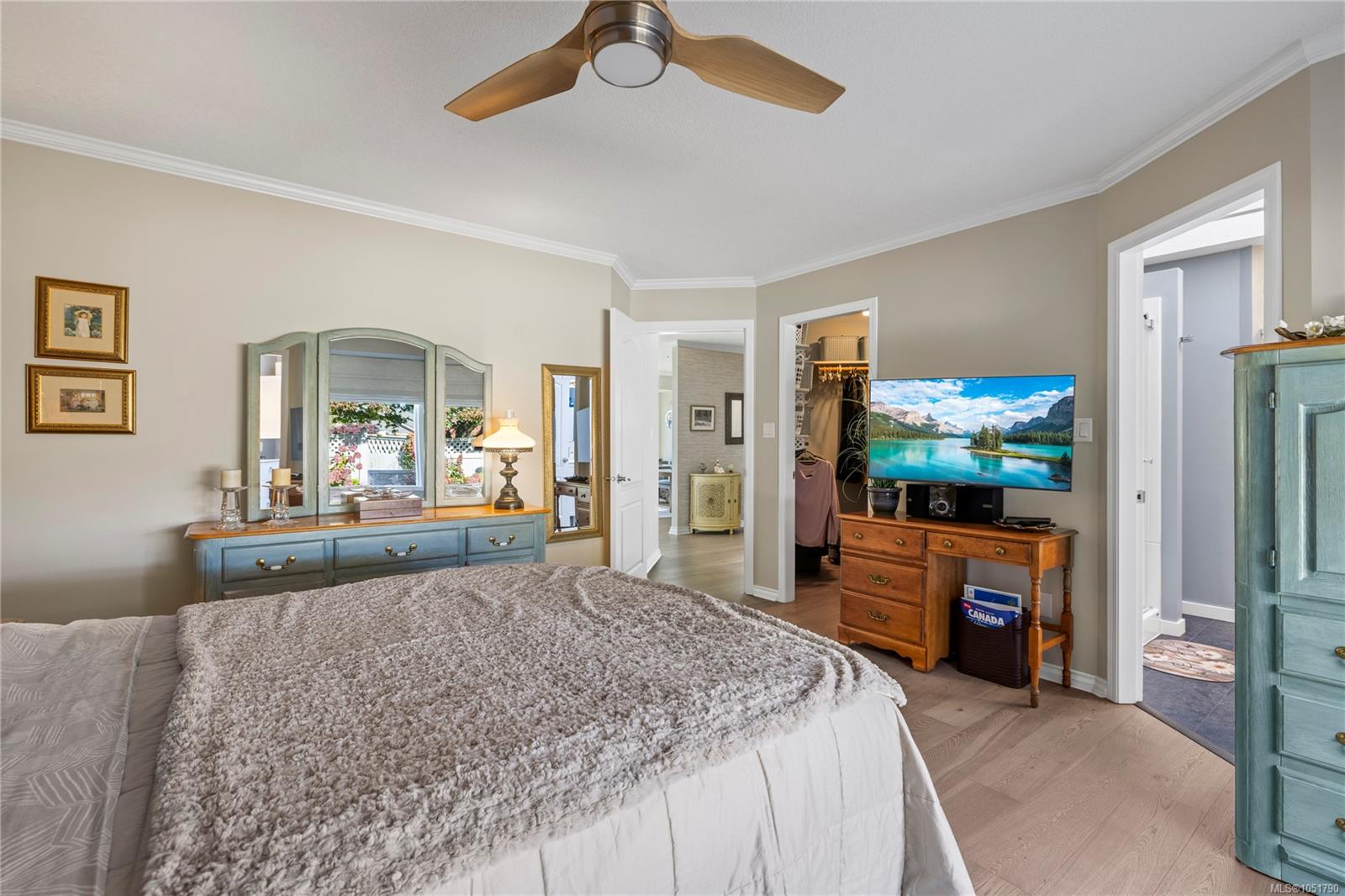 Furnished bedroom with a large bed, mirrored dresser, ceiling fan, and TV beside open closet and bathroom doors.