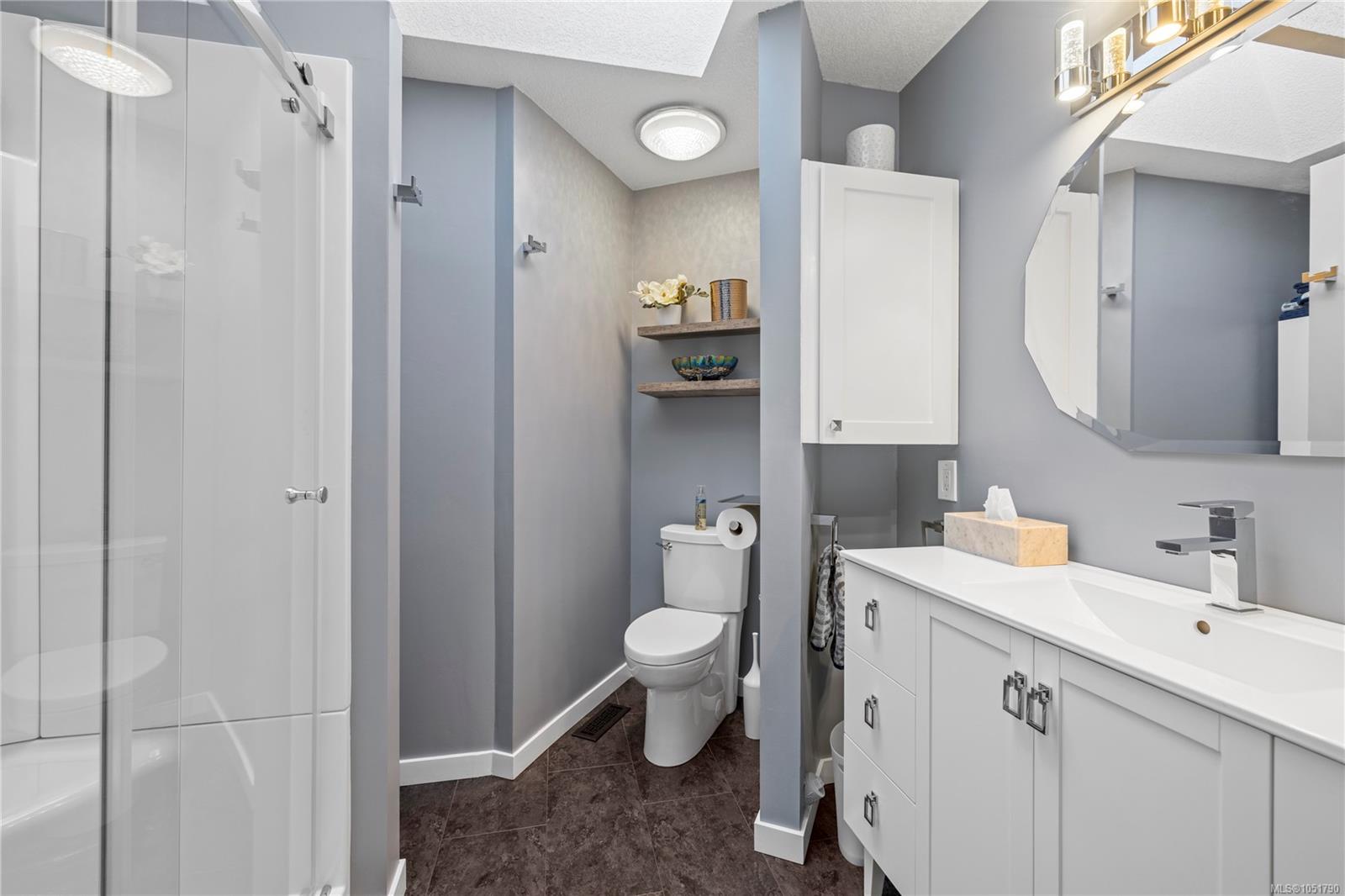Bathroom with a glass shower, white vanity, octagonal mirror, and dark tile floor.