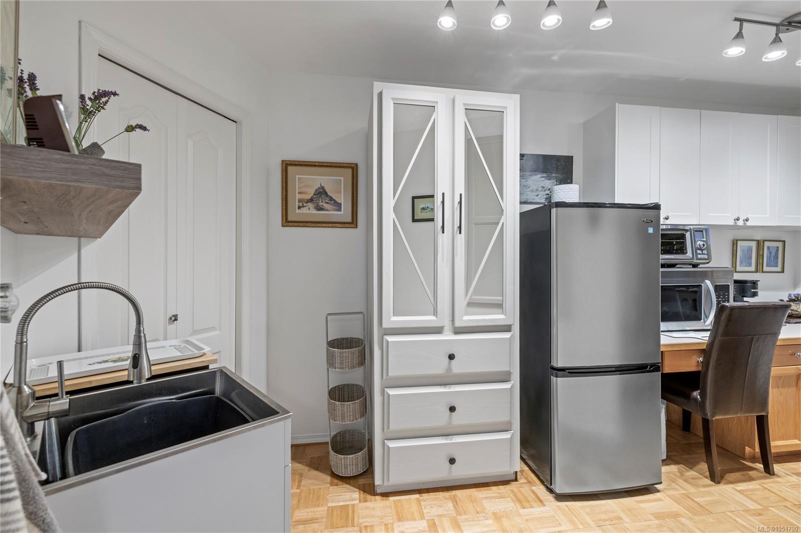 Kitchen with white cabinetry, a black sink, stainless steel refrigerator, and parquet flooring.
