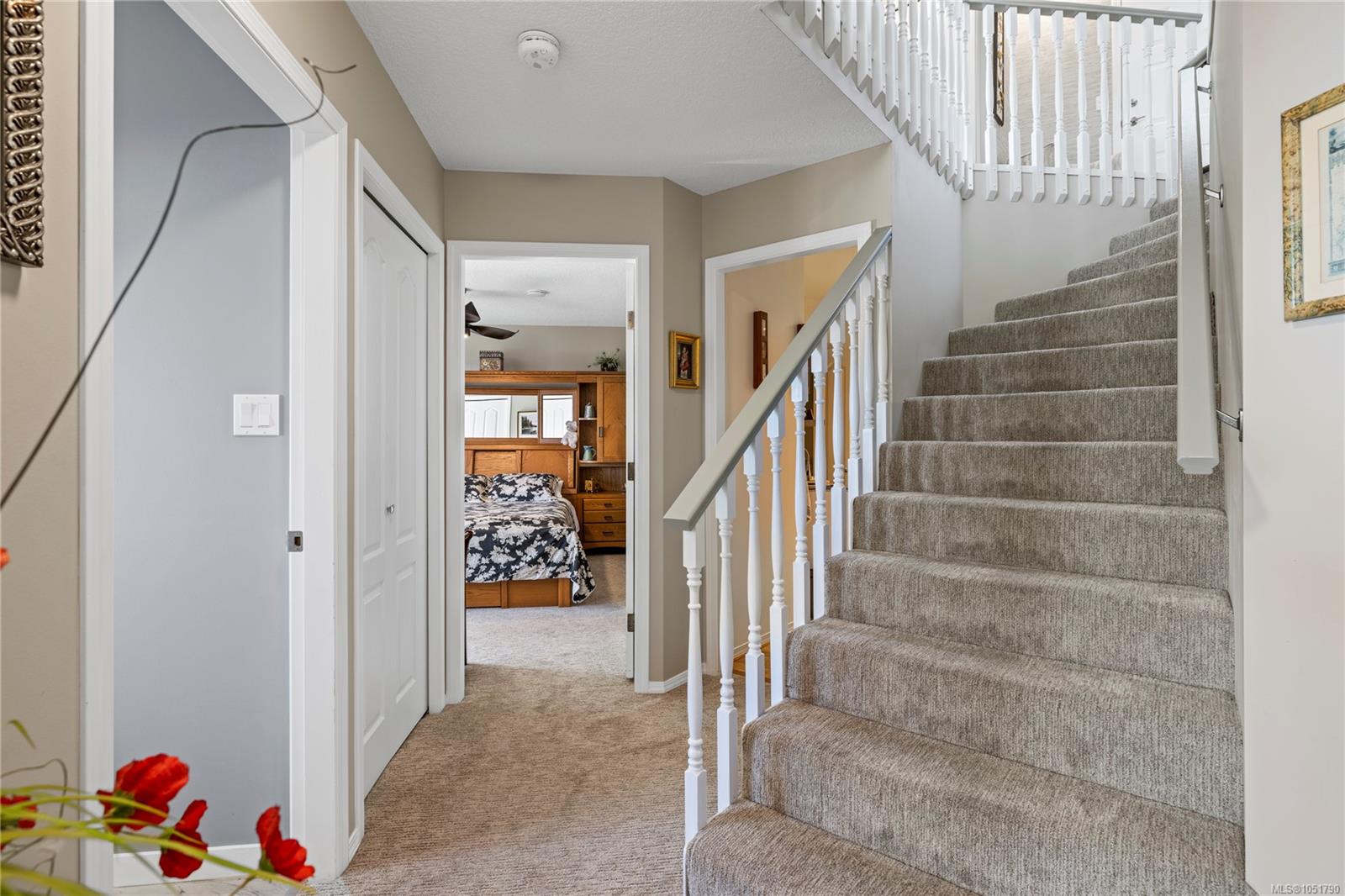 Carpeted staircase and upstairs landing with white railings and a bedroom visible down the hall.