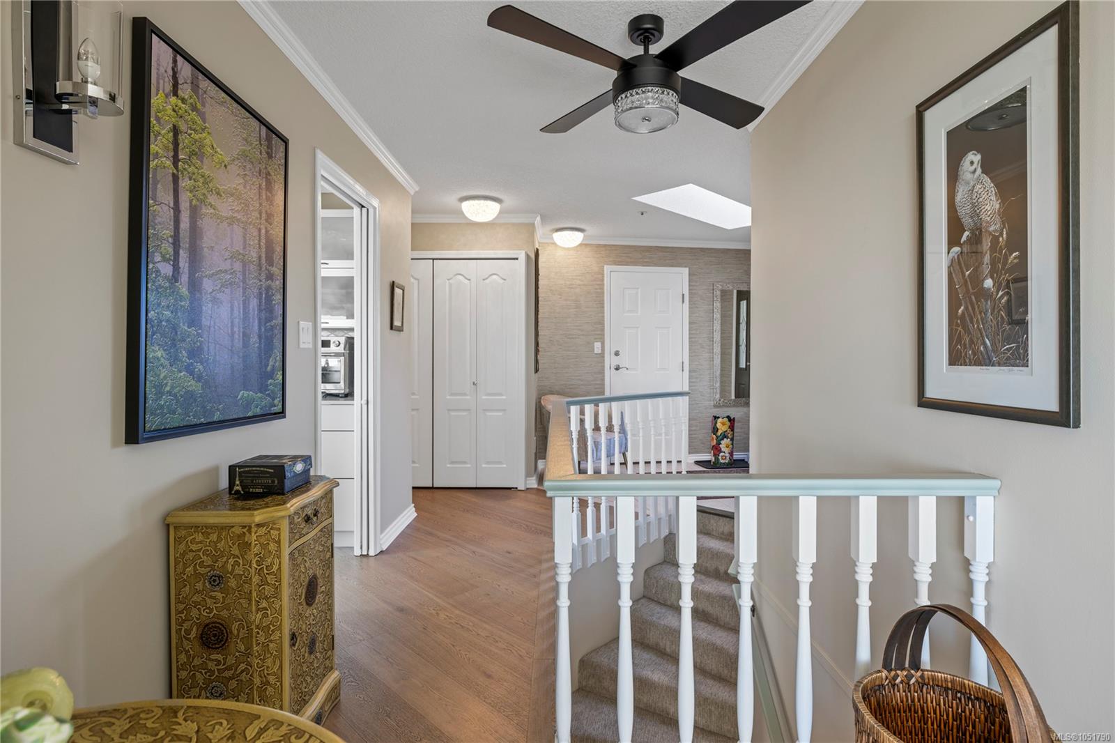 Upstairs landing with hardwood floors, white stair railing, ceiling fan, and skylight.