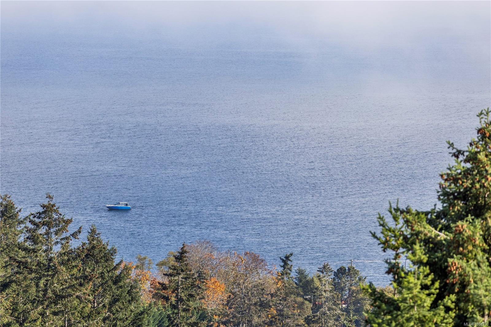 Broad water view with a small boat offshore and autumn-colored trees in the foreground.