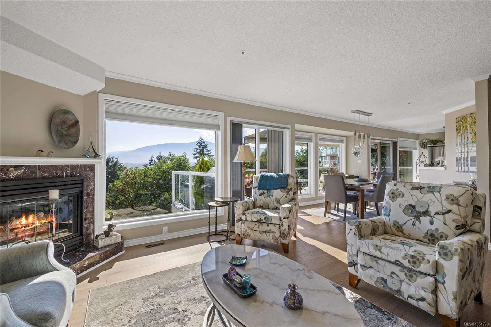 Living room with a fireplace, floral armchairs, and large windows overlooking mountains.