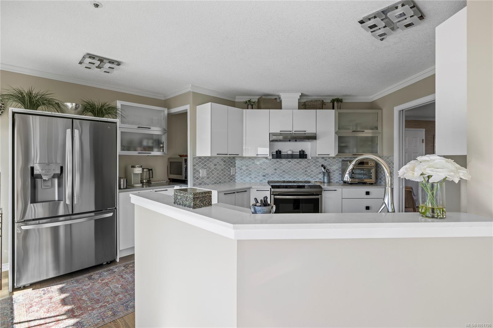 Kitchen with white cabinets, stainless-steel appliances, and a large peninsula with a vase of flowers.