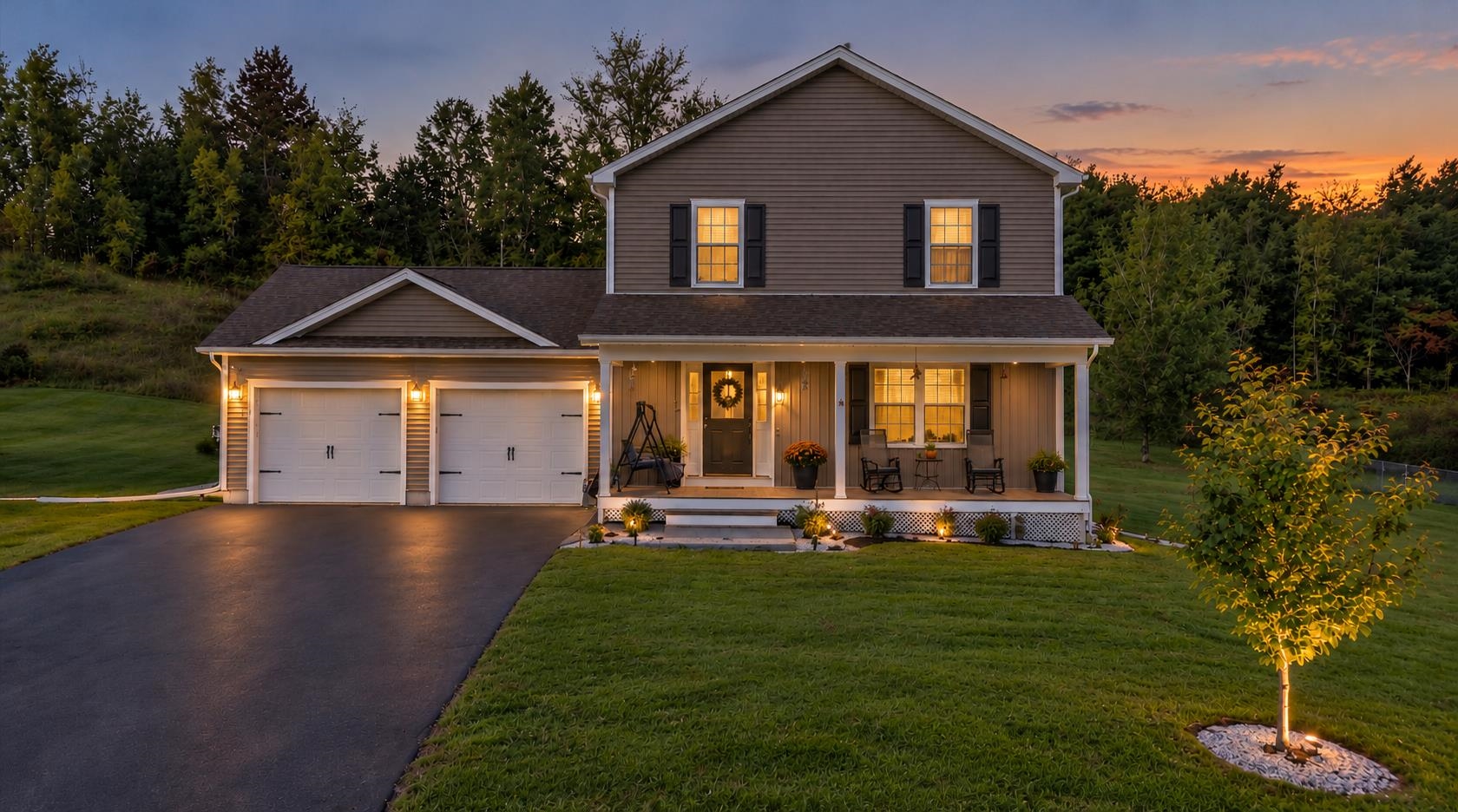 Two-story home with a two-car garage and covered porch, warmly lit at dusk.