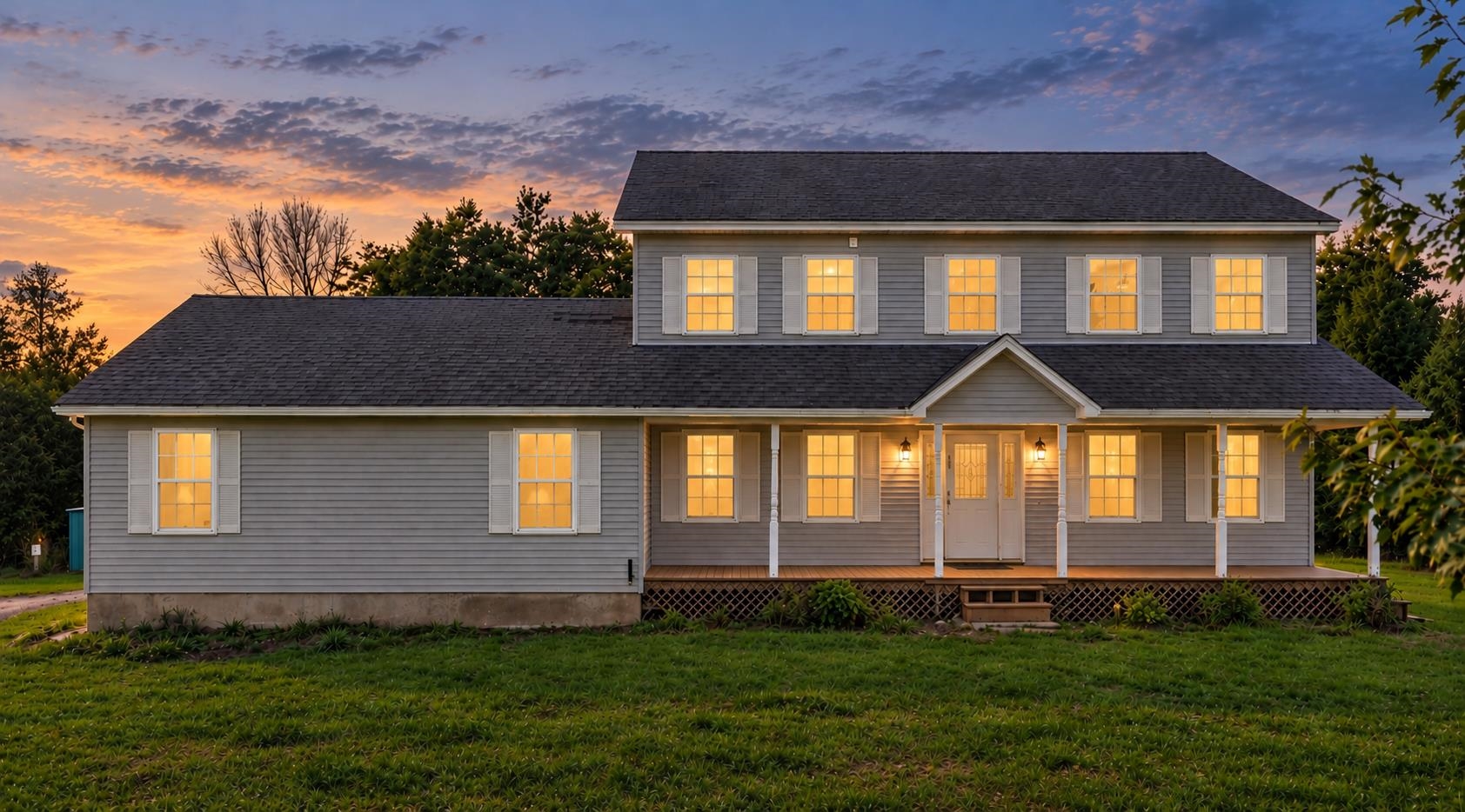 Two-story gray house with a covered porch and glowing windows at dusk.