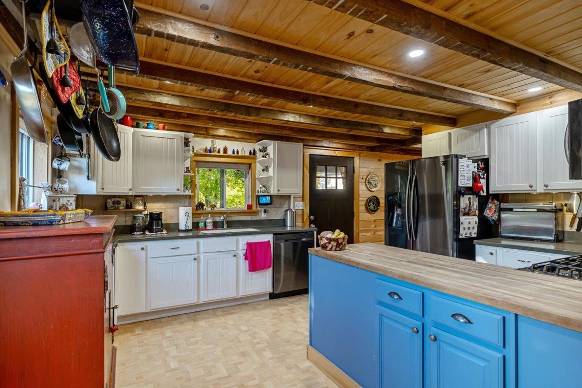 Kitchen with blue island, white cabinets, stainless steel appliances, and exposed wooden ceiling beams.