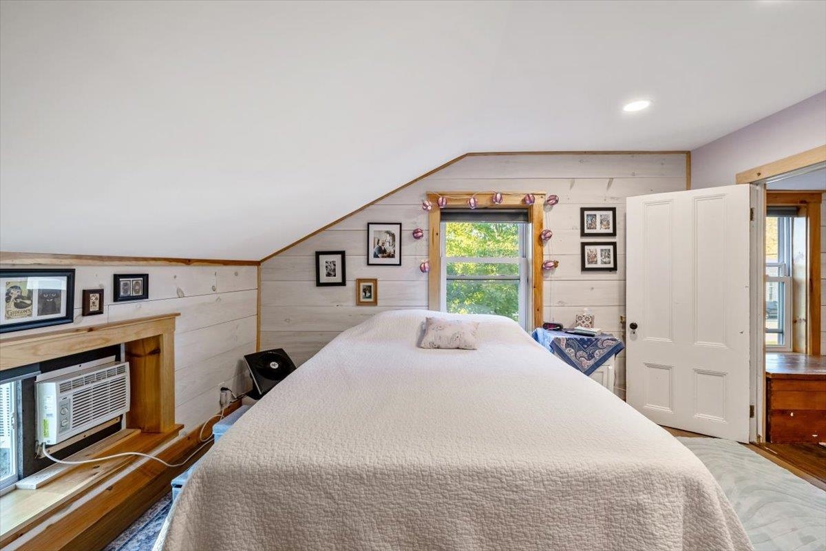 Bedroom with a large bed beneath a sloped ceiling and a window air conditioner.