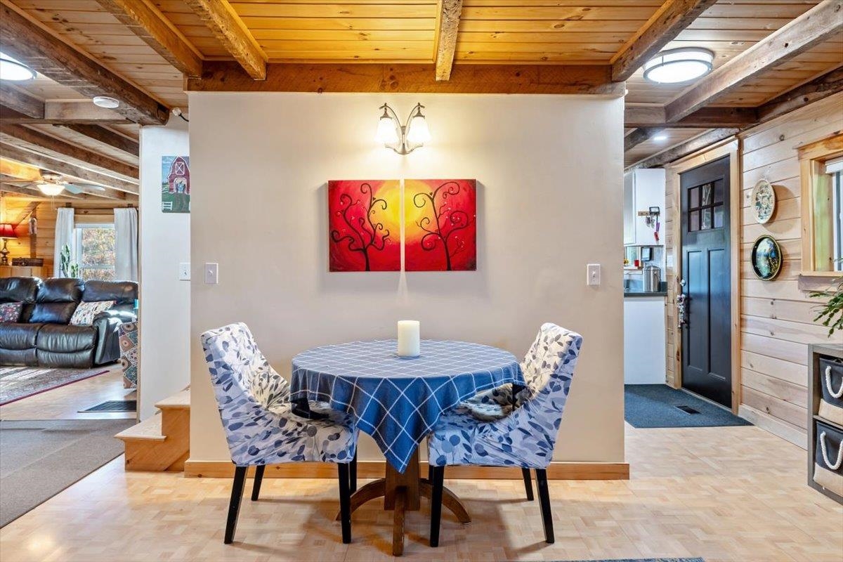 Dining area with a blue-covered round table, patterned chairs, and exposed wood ceiling beams.