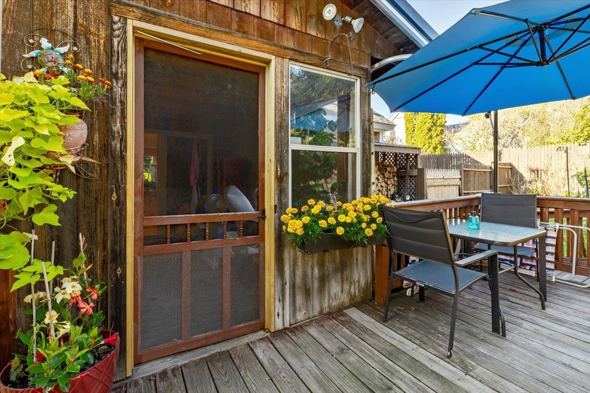 Wooden deck with patio dining set, blue umbrella, and colorful potted flowers beside the house.