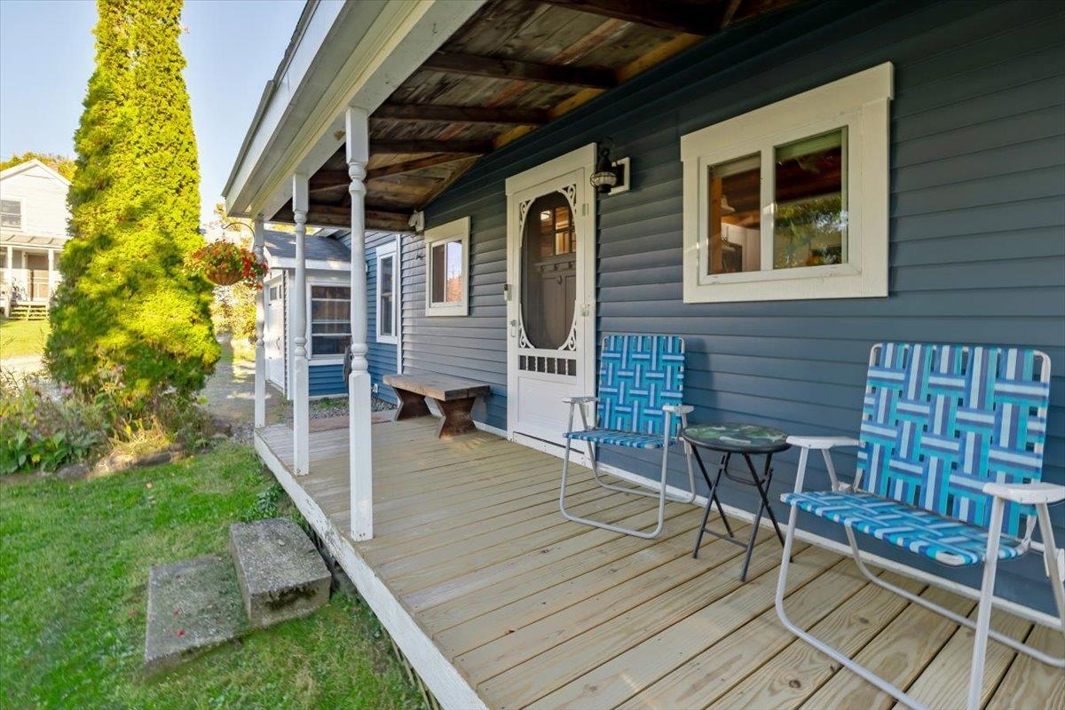 Covered porch with blue patterned chairs, wooden decking, and a decorative white entry door.