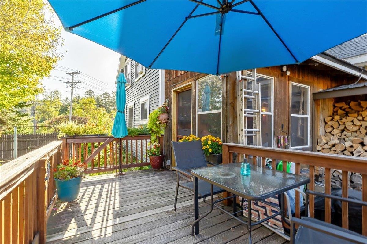 Deck with a glass-top dining table under a large blue umbrella and potted flowers.