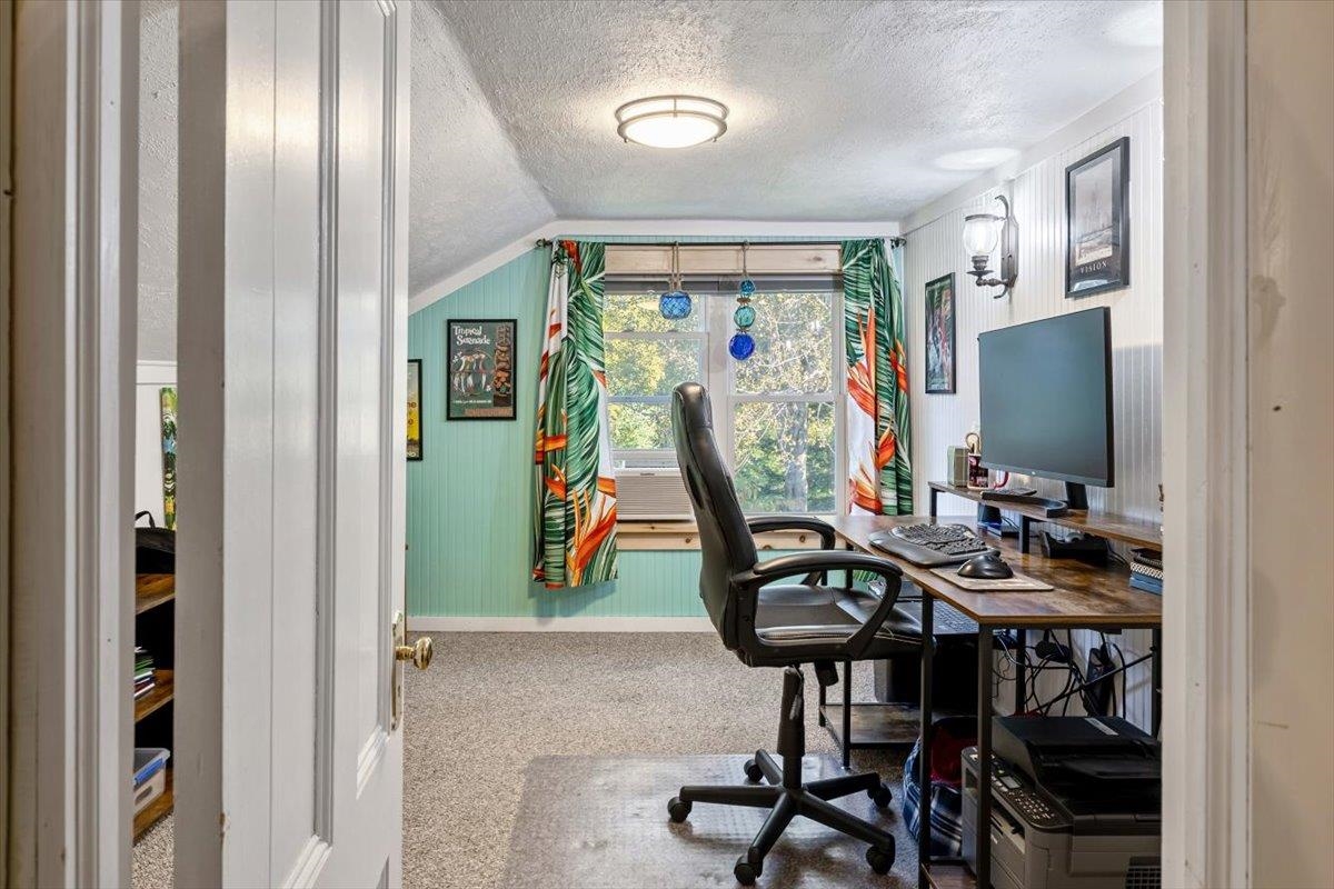 Home office with a computer desk, black chair, mint-green wall, and tropical curtains.