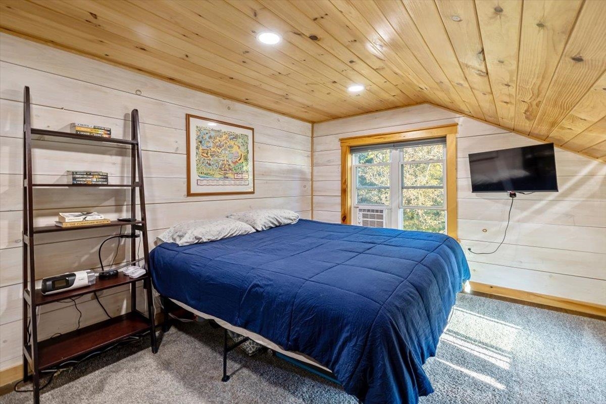 Bedroom with a navy quilted bed beneath a sloped wood ceiling and a sunny window.