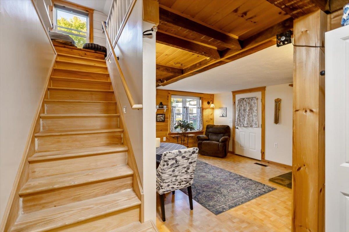 Living area with a broad wooden staircase, exposed ceiling beams, parquet flooring, and an armchair.