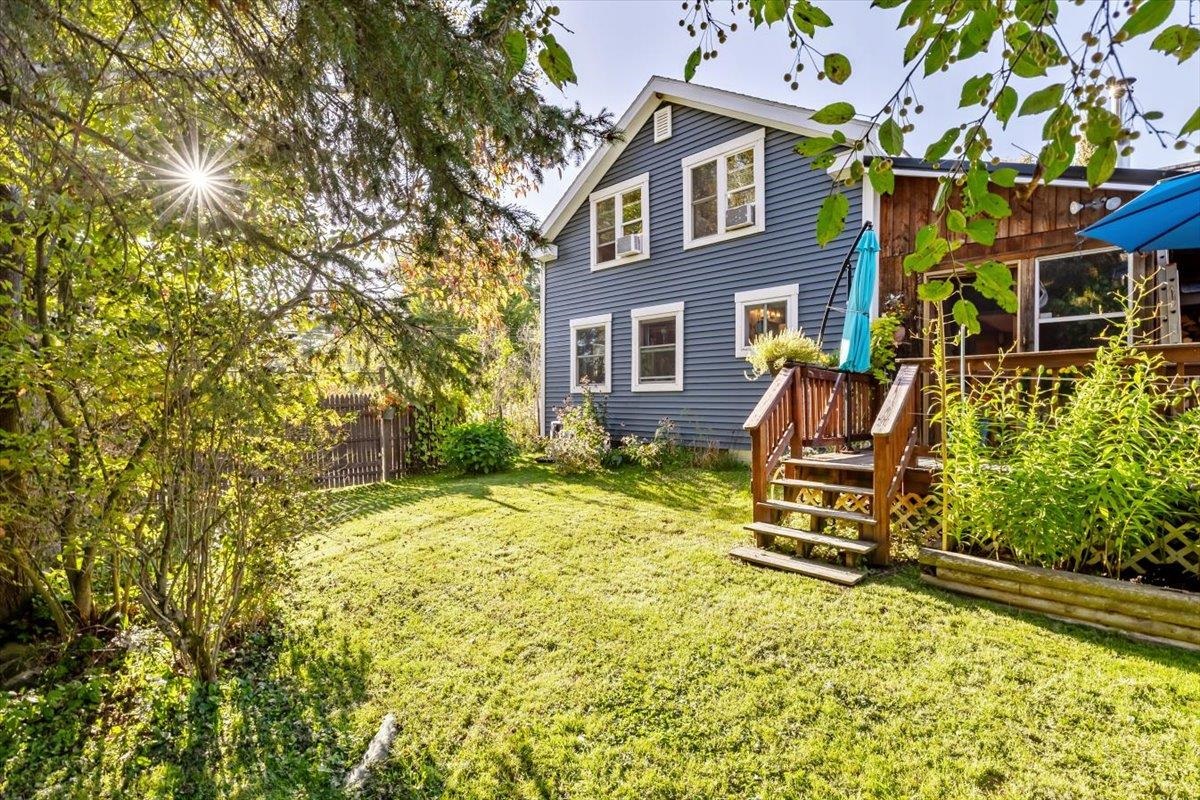 Blue two-story house overlooking a sunny lawn, with a raised wooden deck and leafy trees.