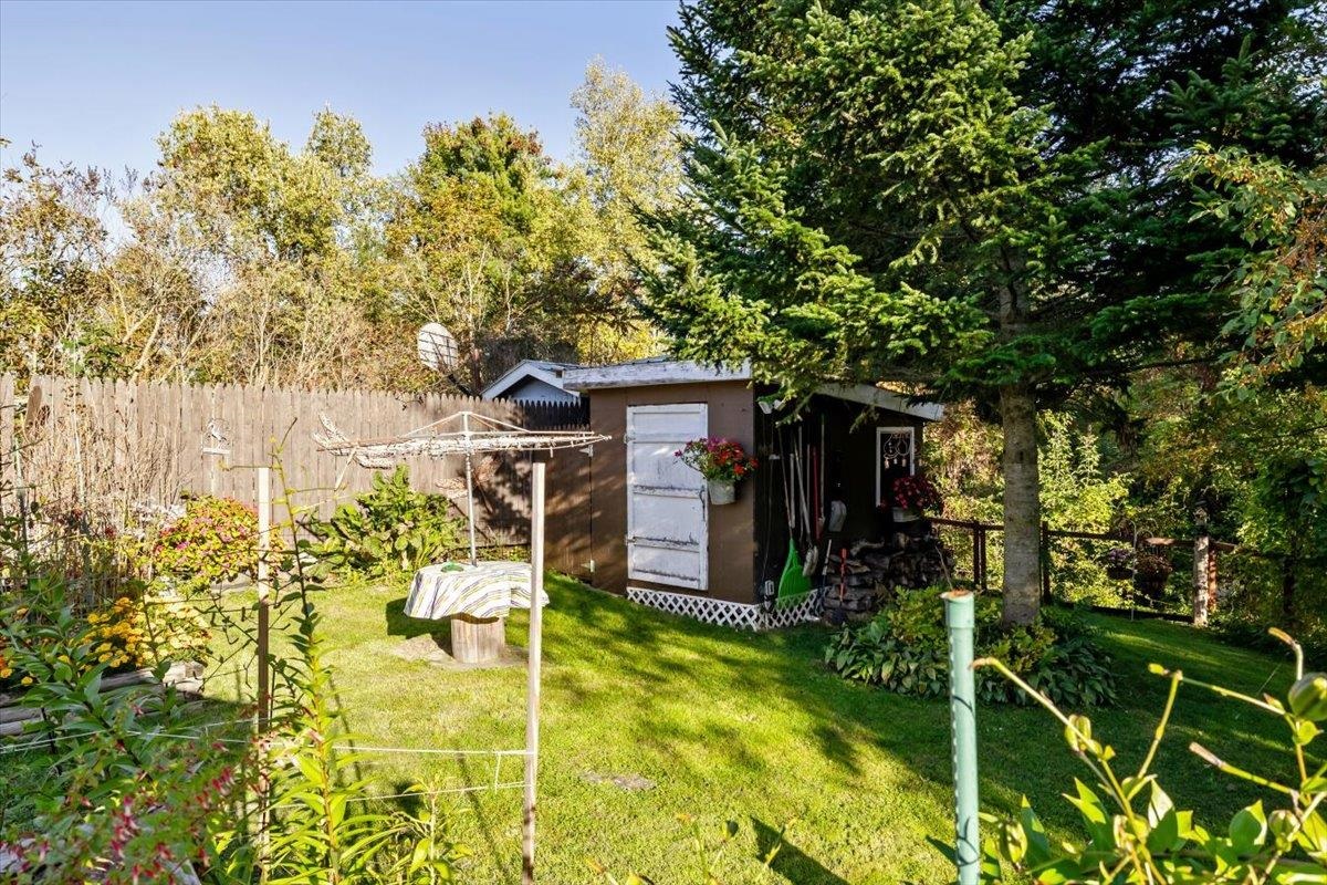 Backyard with a brown shed, clothesline, wooden fence, and mature trees.