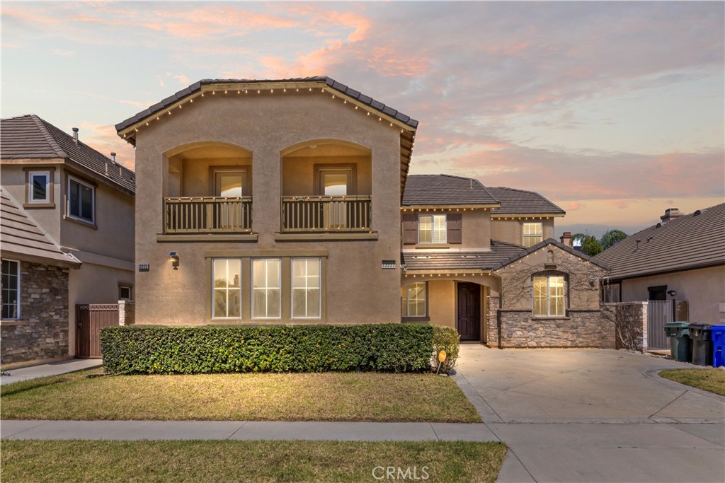 Two-story stucco home with upper balconies, a stone-accented entry and a trimmed front hedge.